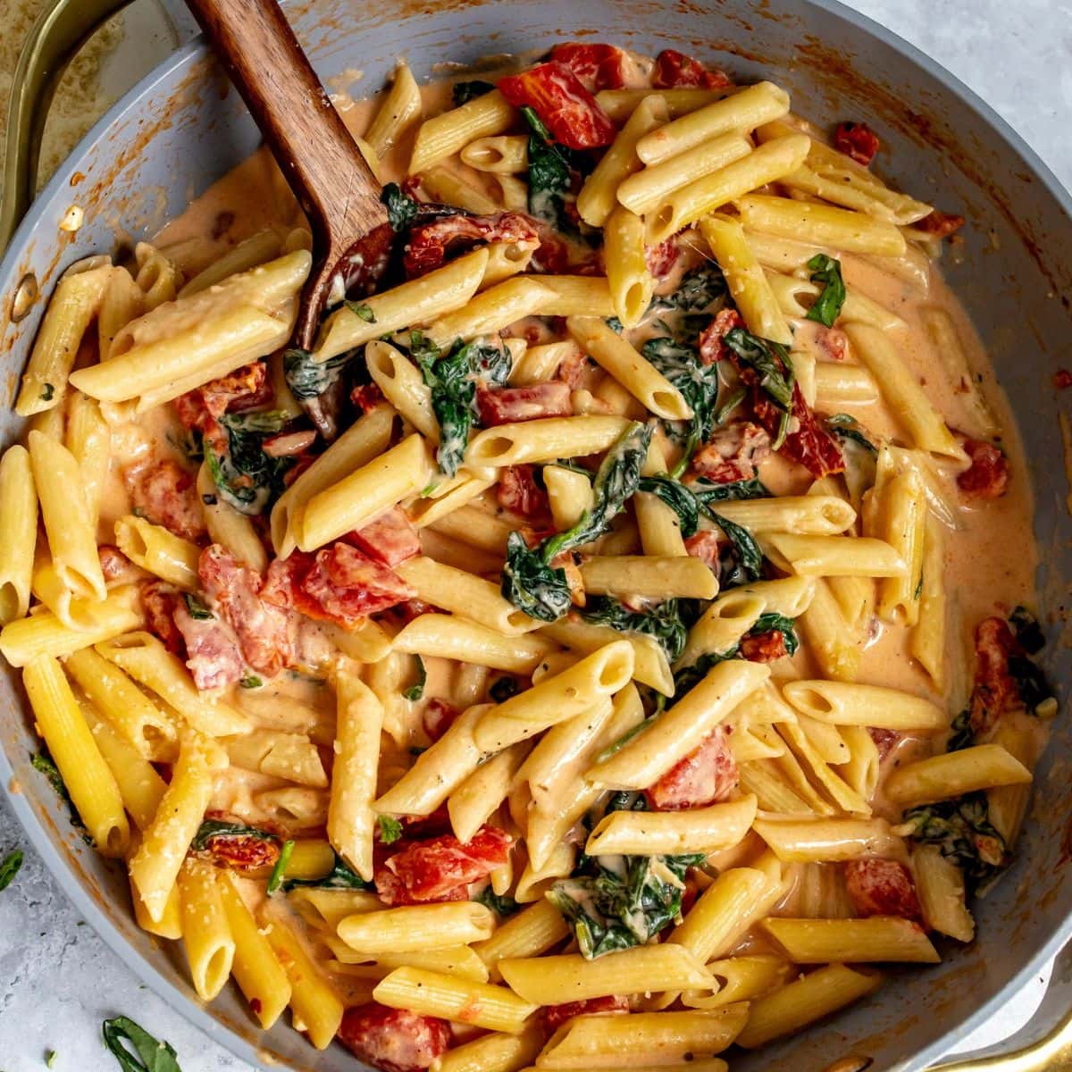 Creamy Tomato Spinach Pasta in a grey skillet with a spoon.