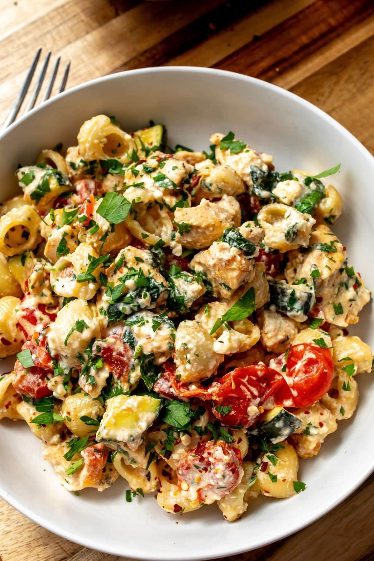 Ceramic bowl with feta cheese chicken bake in it, topped with parsley and a silver fork to the side.