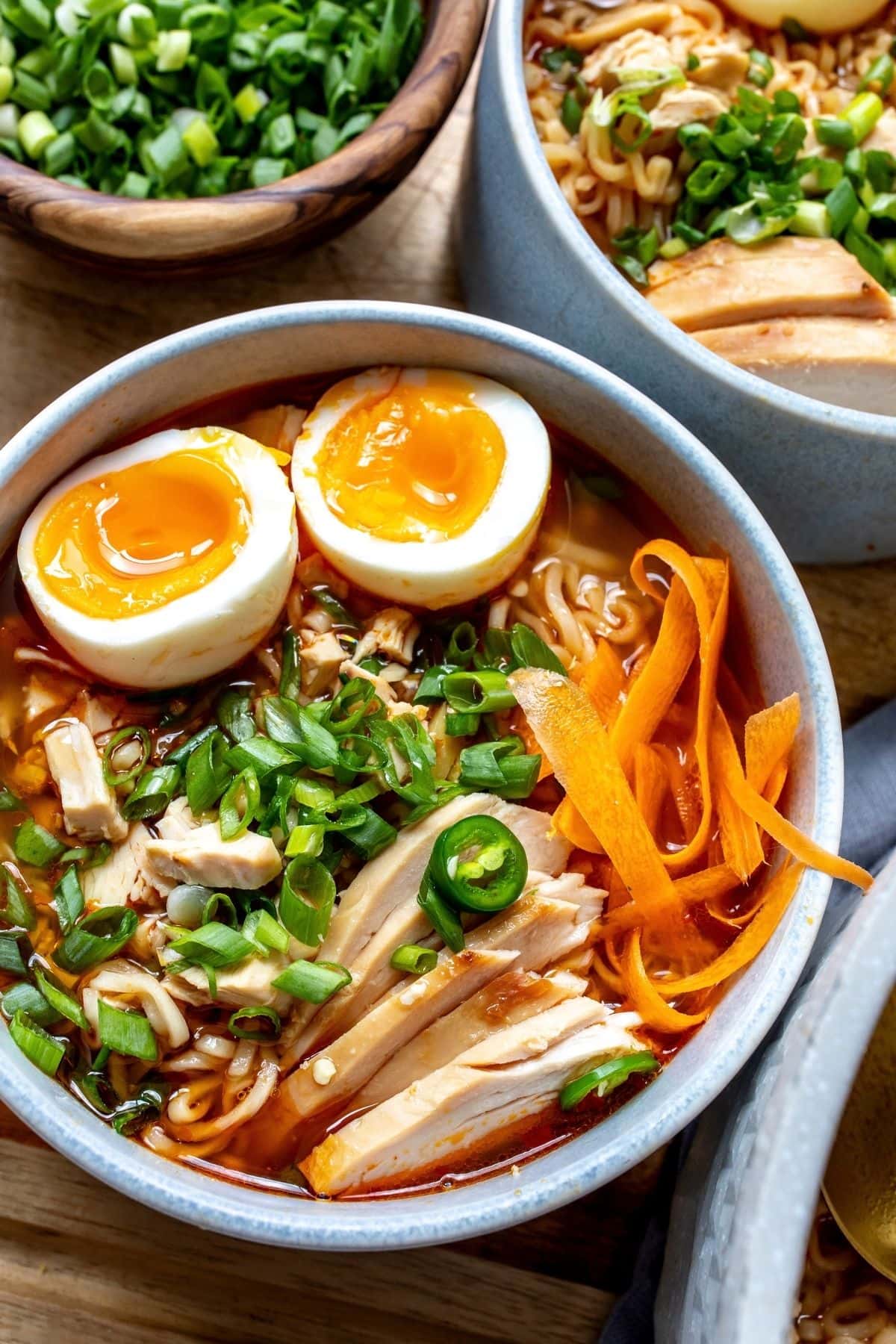 Spicy Chicken Ramen in broth served in white grey bowls with toppings.
